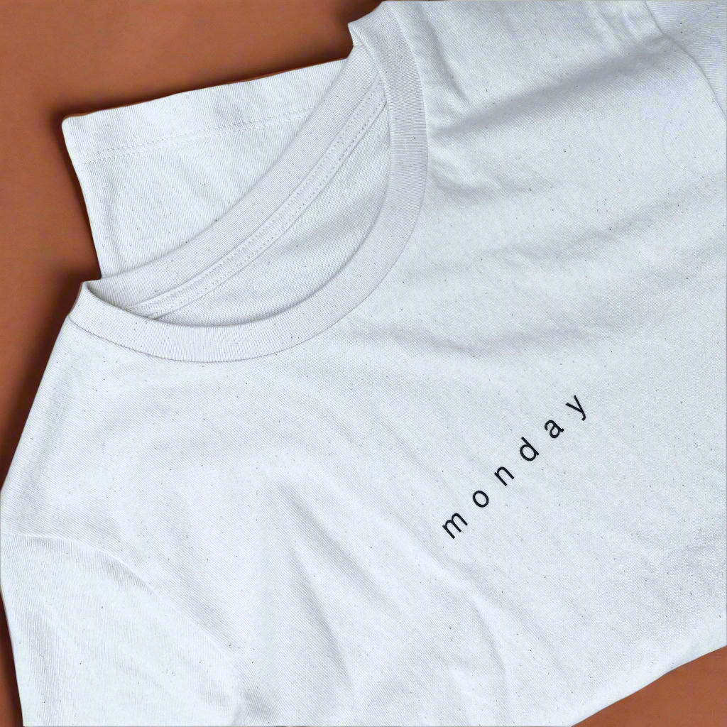 White t-shirt with 'monday' text on a brown surface