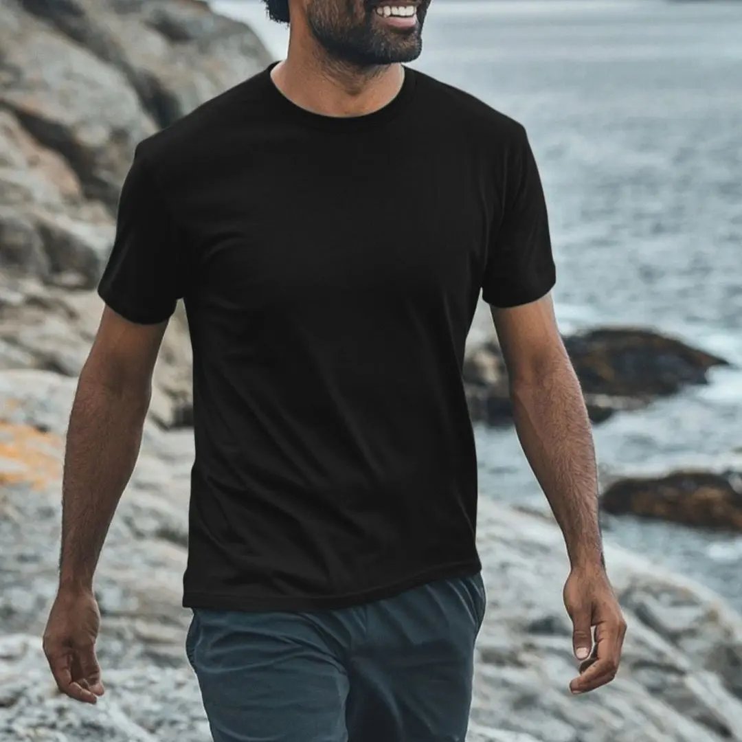 Man wearing a black t-shirt and gray shorts walking along a rocky shoreline.