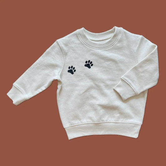 White sweatshirt with black paw prints on a brown background