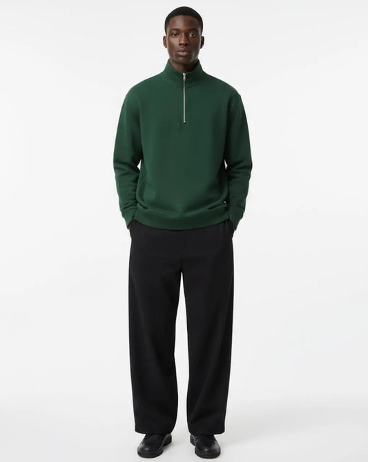 Man wearing a green quarter-zip sweatshirt and black pants on a white background