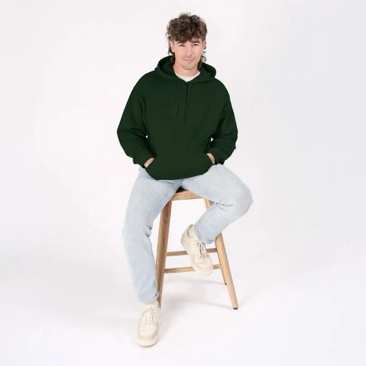 Person wearing a green hoodie and light gray pants sitting on a wooden stool against a white background