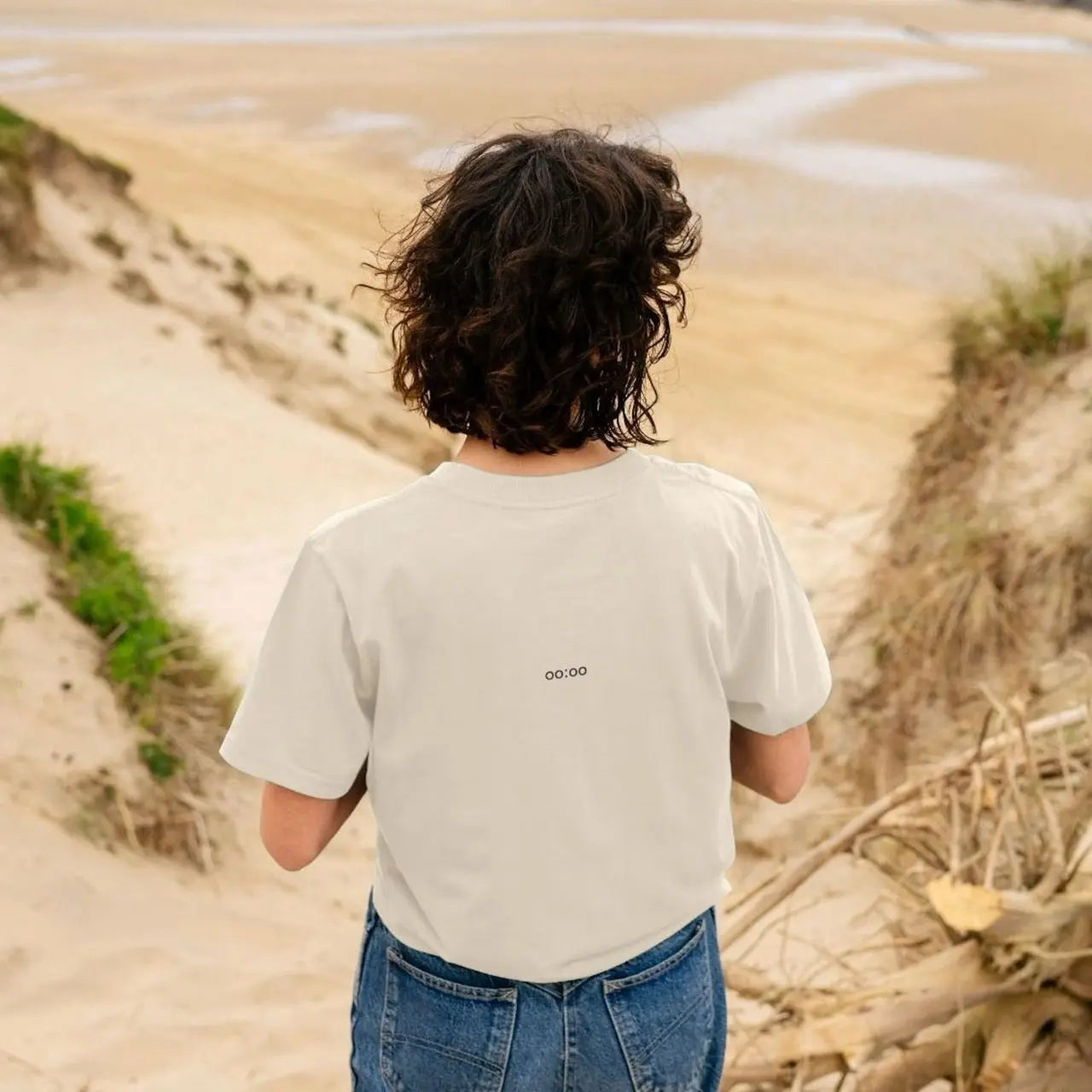 Person wearing a beige t-shirt with text, standing in a desert-like landscape.