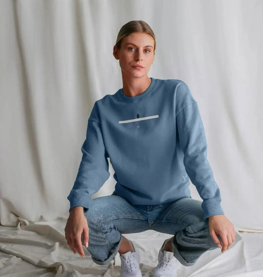 Woman wearing a blue sweatshirt and jeans sitting on a white surface with a white curtain background