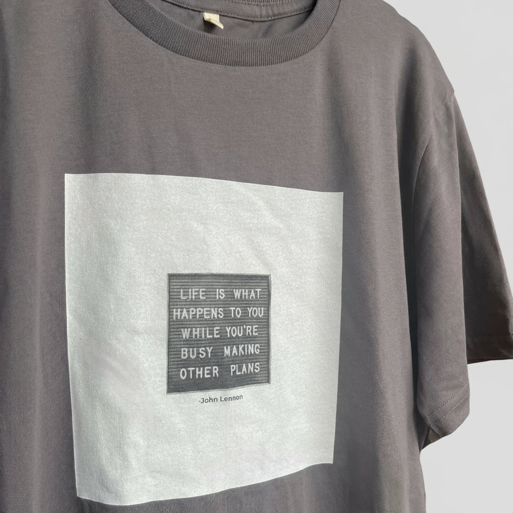 Dark gray t-shirt with a white square and John Lennon quote in a smaller gray square printed on the chest