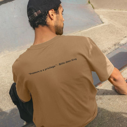 Person wearing a brown t-shirt with a quote on it, sitting on a stone surface.