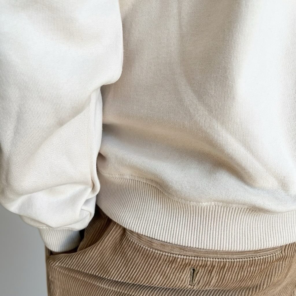 Close-up of beige sweatshirt and brown pants against a neutral background