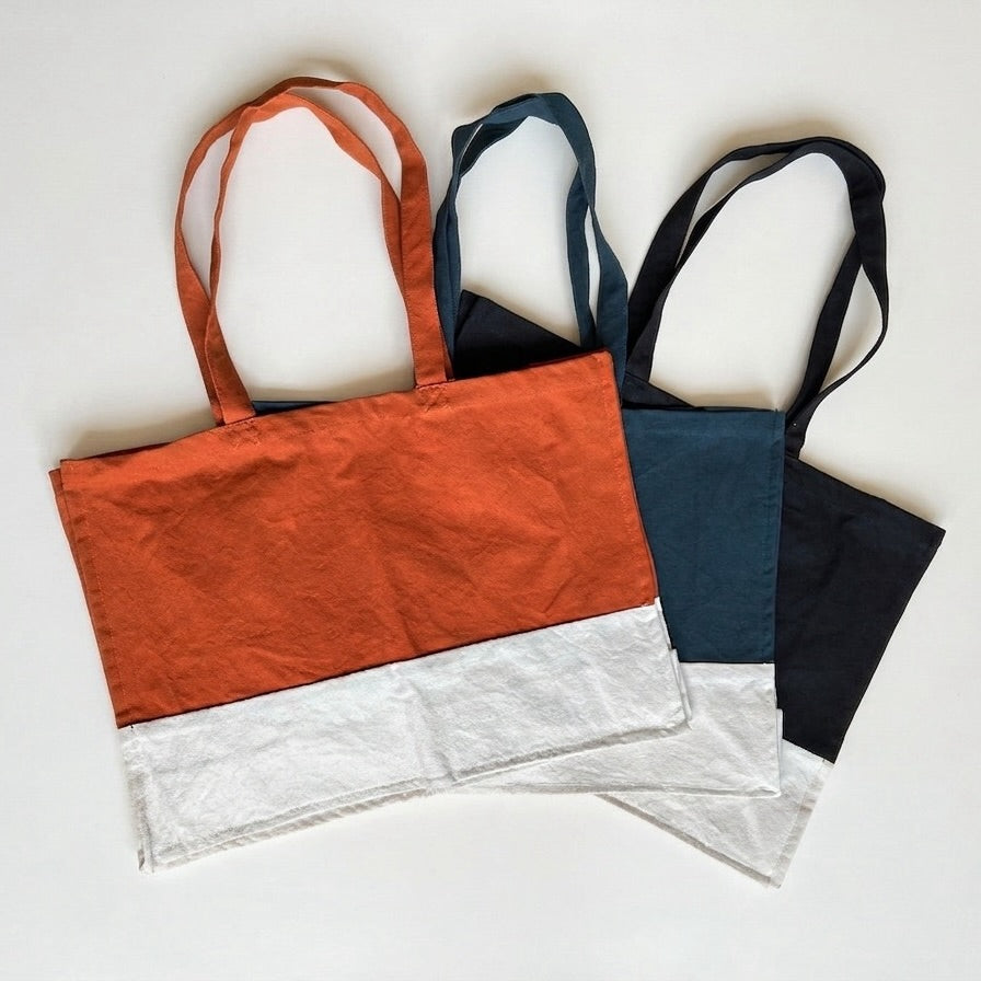 three organic cotton canvas bags, one orange, one black, and one blue, on a white background