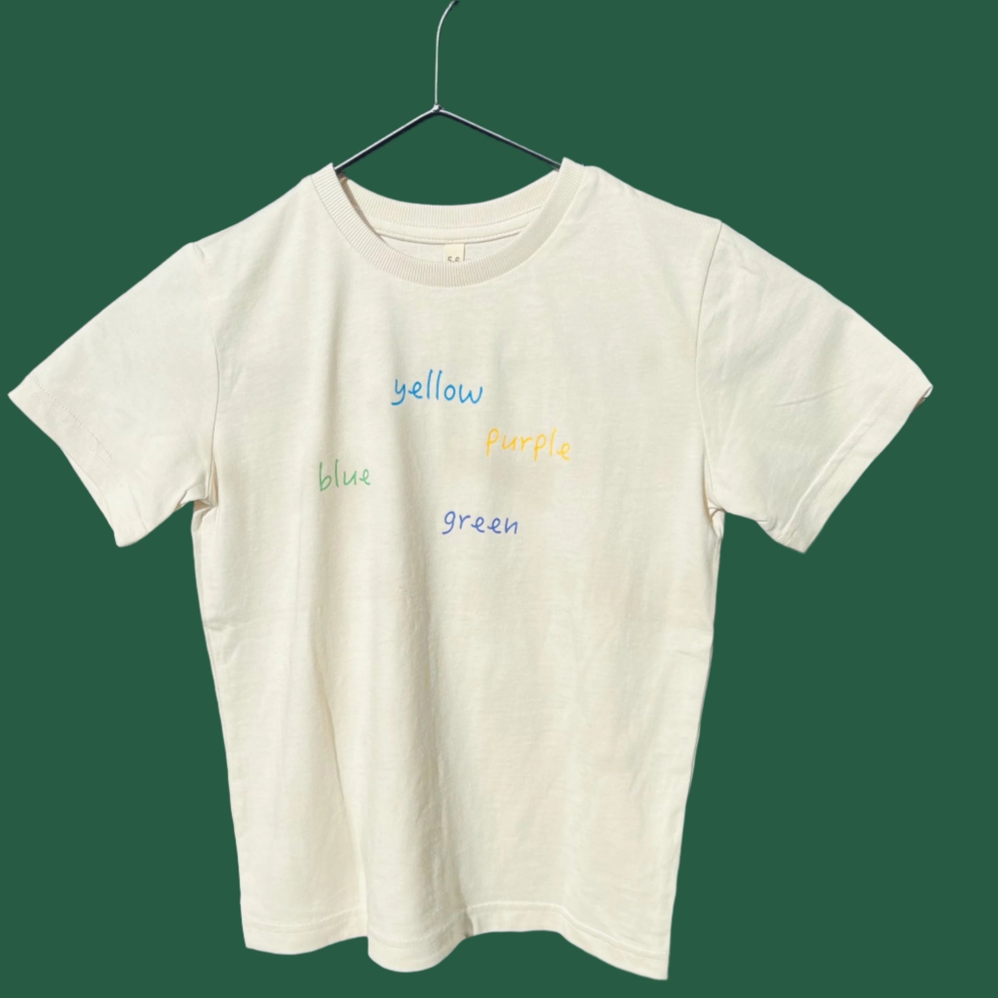 A oat cream kids' organic cotton tee with colorful text 'yellow blue green' printed across the front