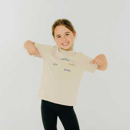 Child wearing a beige t-shirt with color words