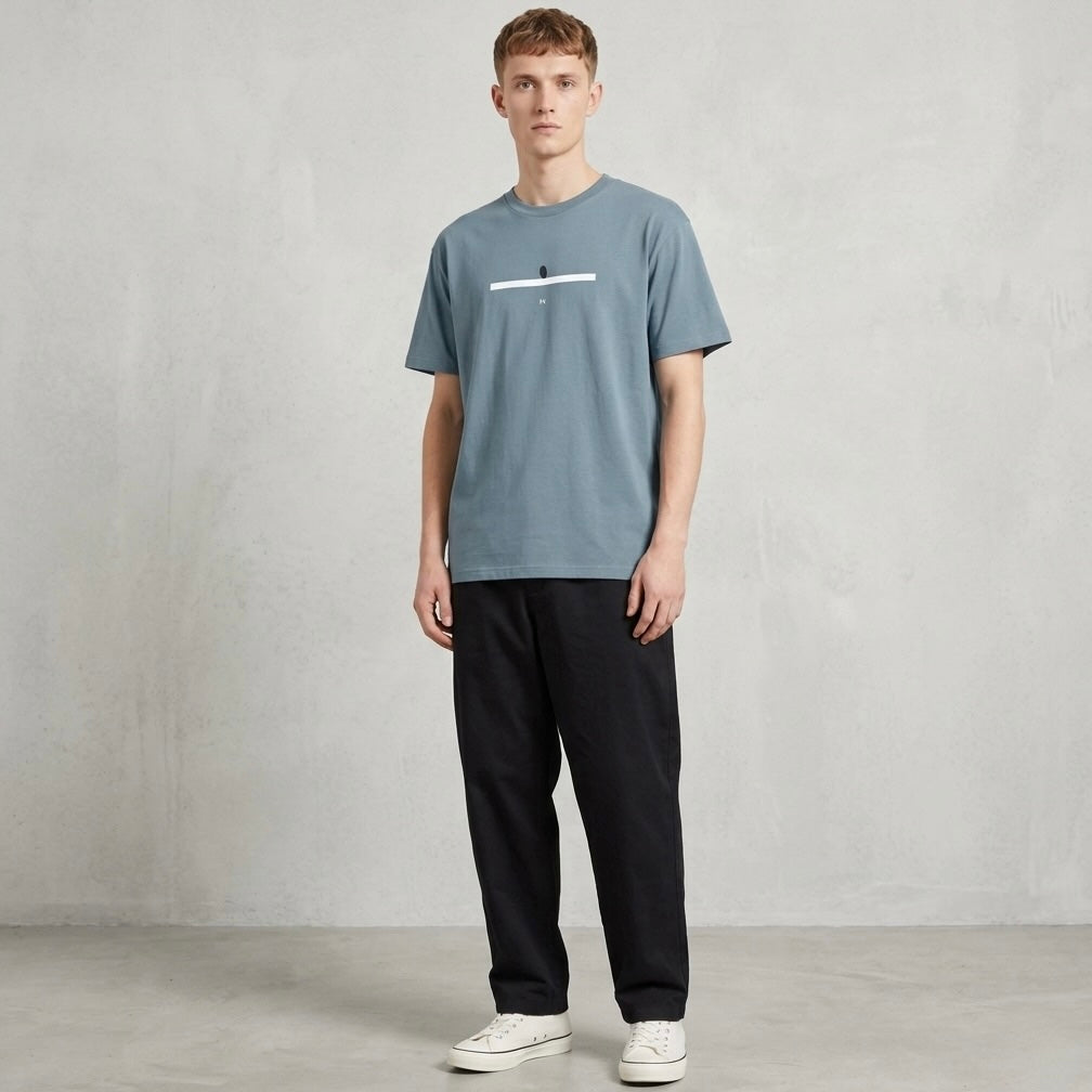 Man wearing a stone blue t-shirt and black pants against a plain background