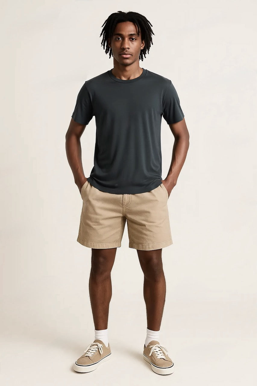 Man wearing a dark gray t-shirt and beige shorts against a plain background