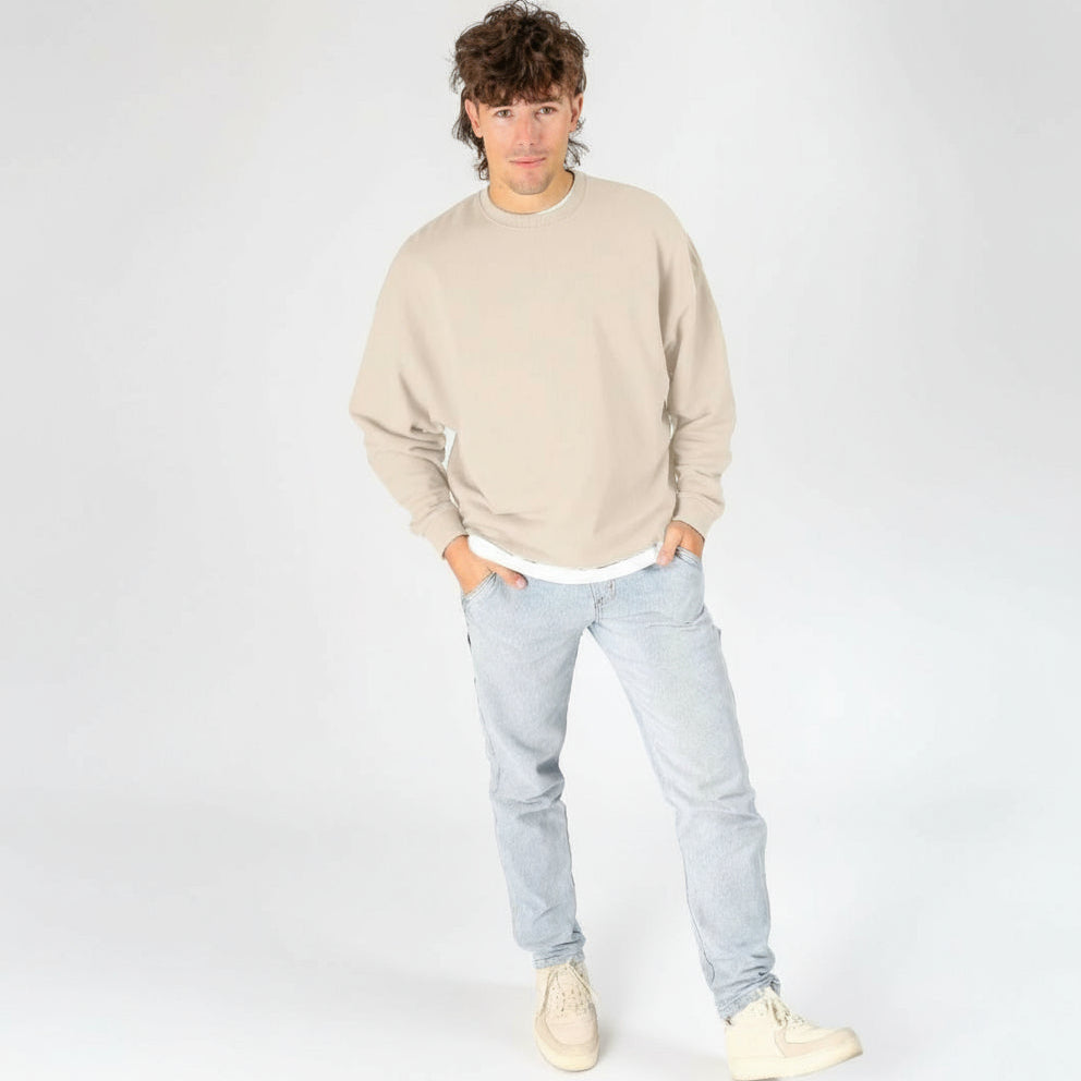 Person wearing a beige sweatshirt and light blue jeans on a white background