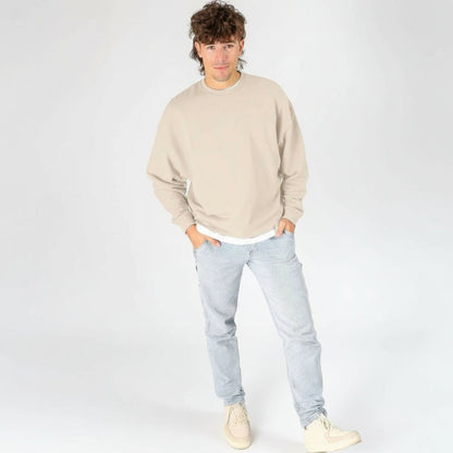 Person wearing a beige sweatshirt and light blue jeans on a white background