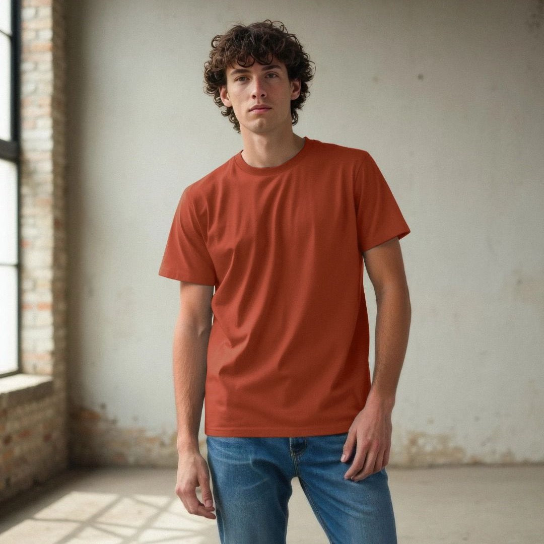Man wearing a red t-shirt and blue jeans standing in a room with brick walls and large windows.