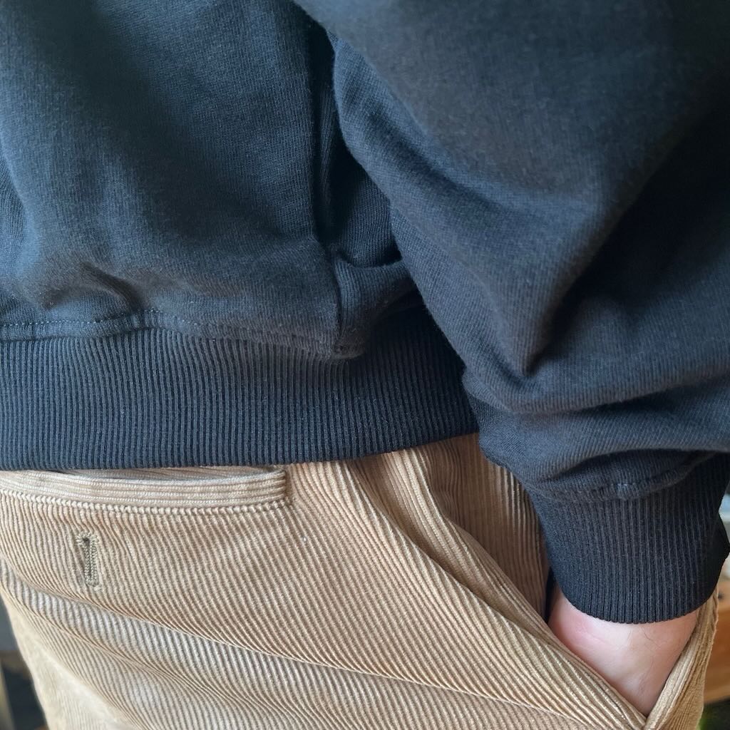Person wearing a dark blue hoodie and beige pants with a blurred background