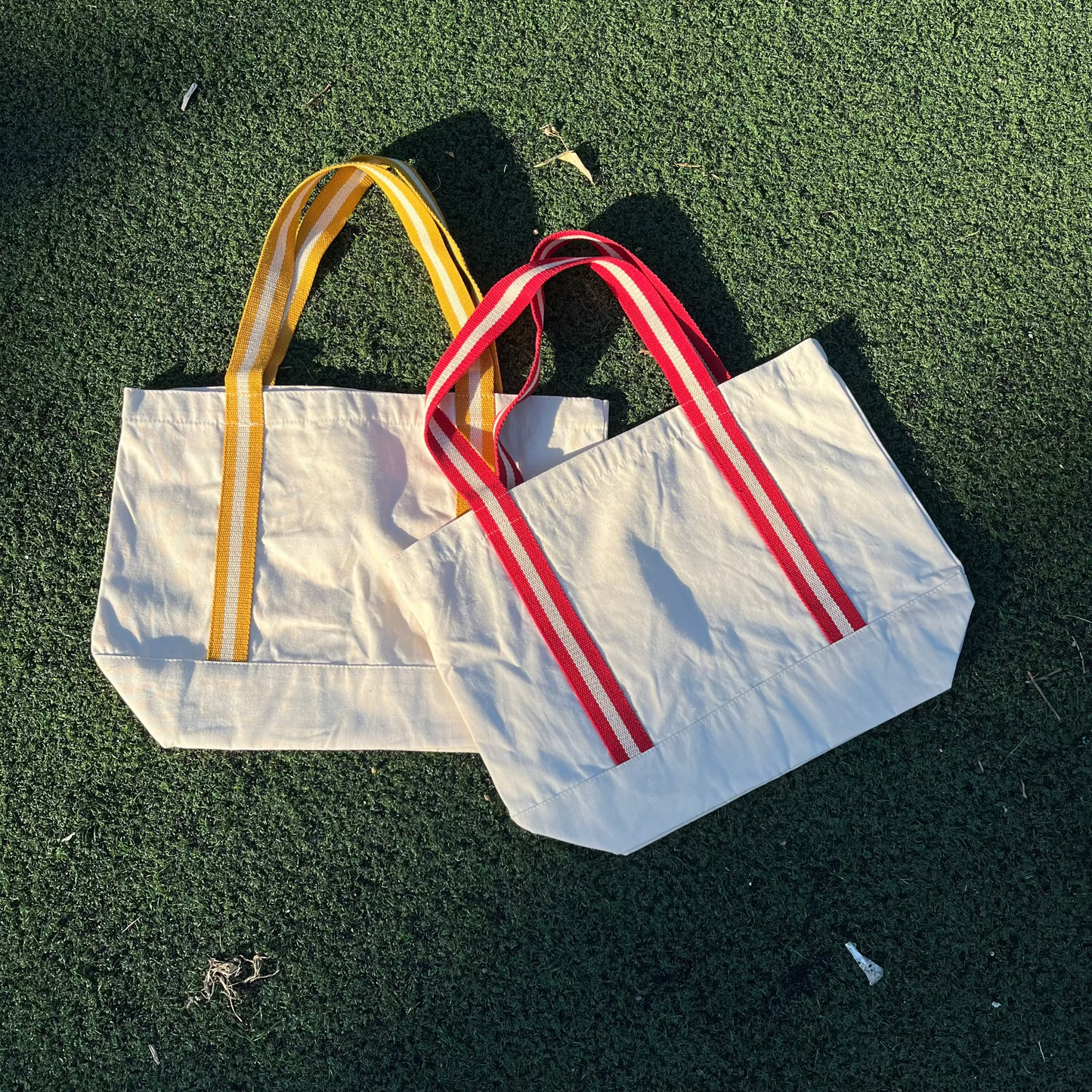 Two tote bags with yellow and red handles on a green grass background