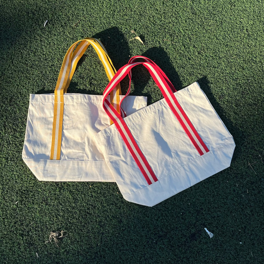 Two tote bags with yellow and red handles on a green grass background