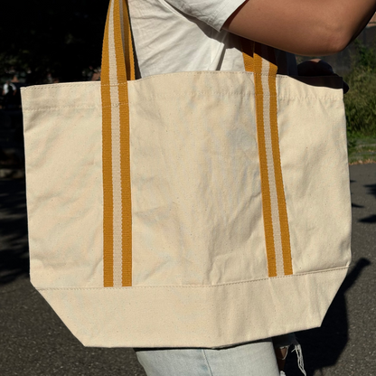 Person holding a beige tote bag with yellow stripes outdoors
