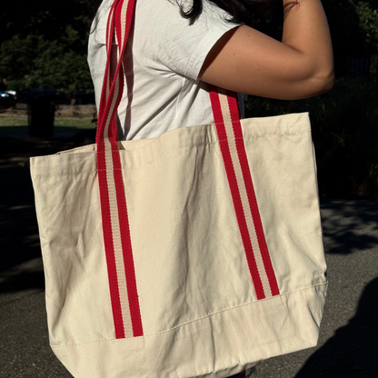 Beige tote bag with red stripes held by a person outdoors