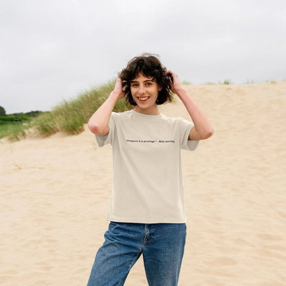 Person wearing a beige t-shirt with text on it, standing on a sandy dune.