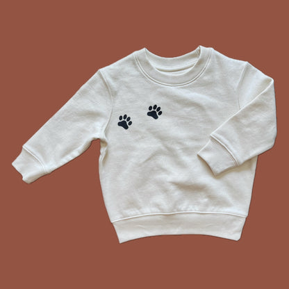 A natural raw colored organic cotton sweatshirt for kids with black paw prints on the chest.