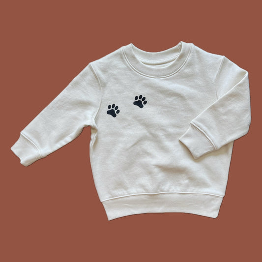 A natural raw colored organic cotton sweatshirt for kids with black paw prints on the chest.