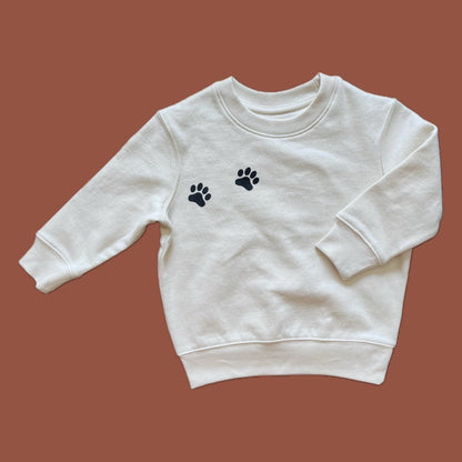 White sweatshirt with black paw prints on a brown background