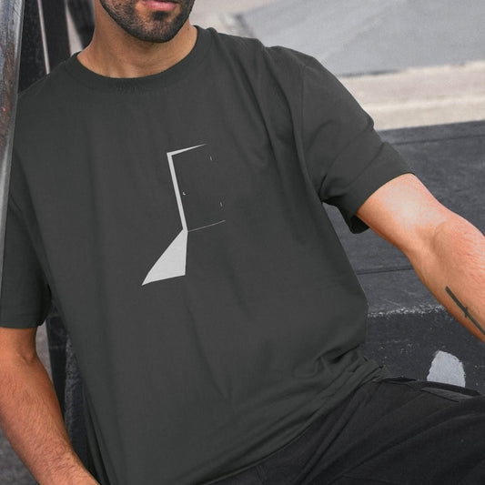 Man wearing a black t-shirt with a white geometric design, sitting against a blurred background.