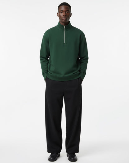 Man wearing a green quarter-zip sweatshirt and black pants on a white background