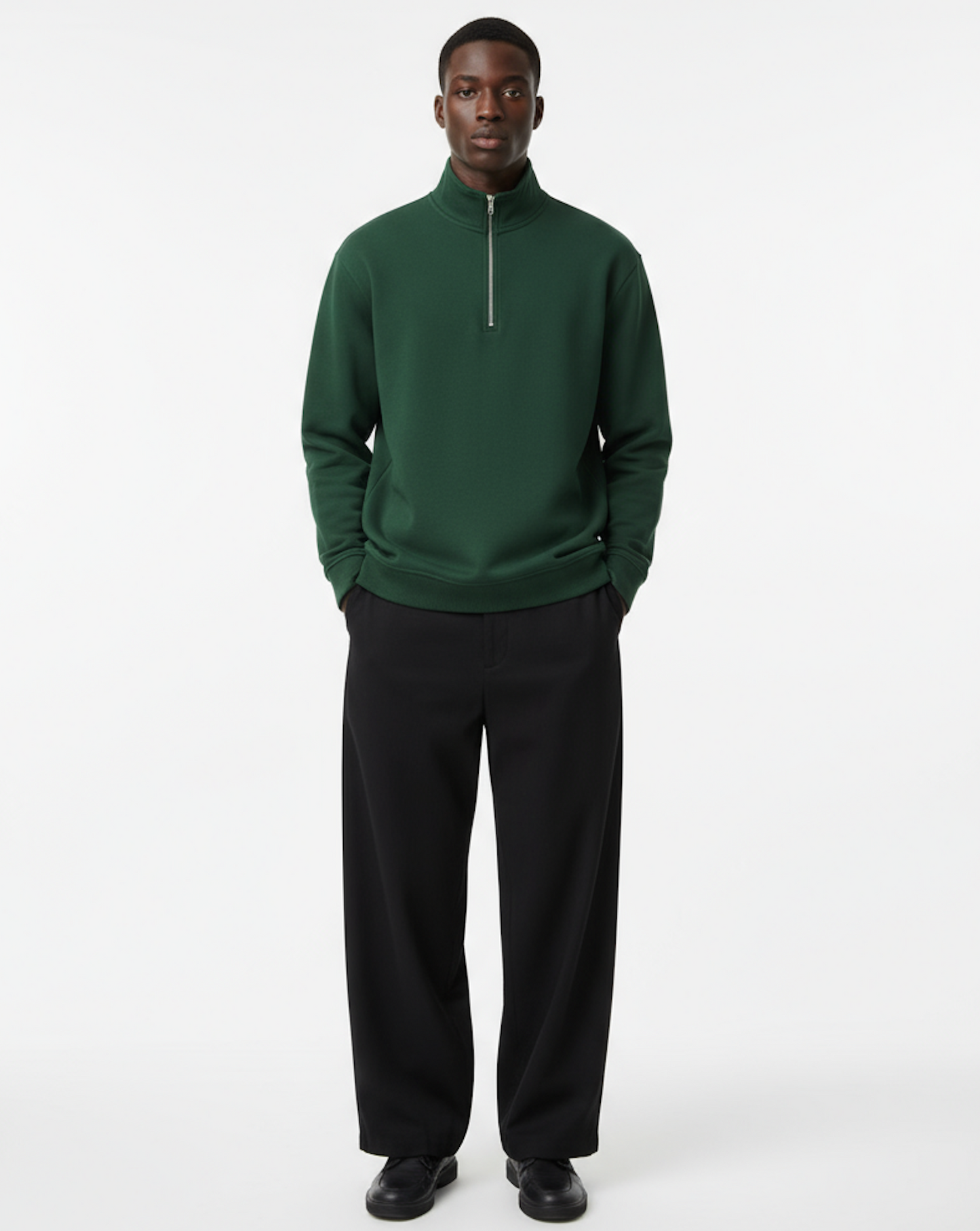 Man wearing a green quarter zip sweater and black pants on a white background
