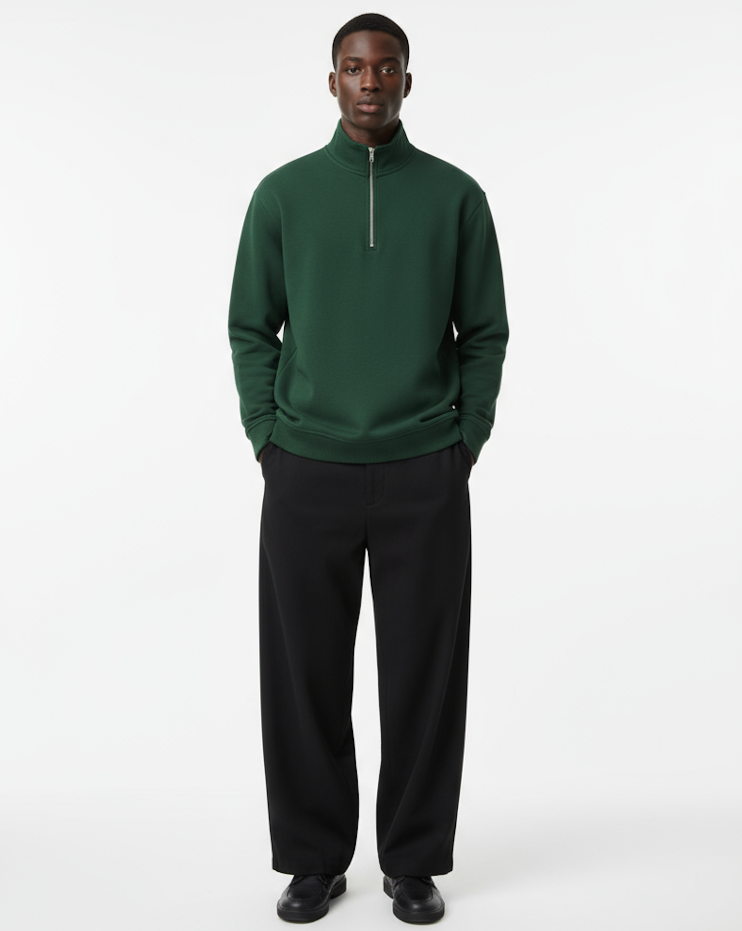 Man wearing a green quarter zip sweater and black pants on a white background