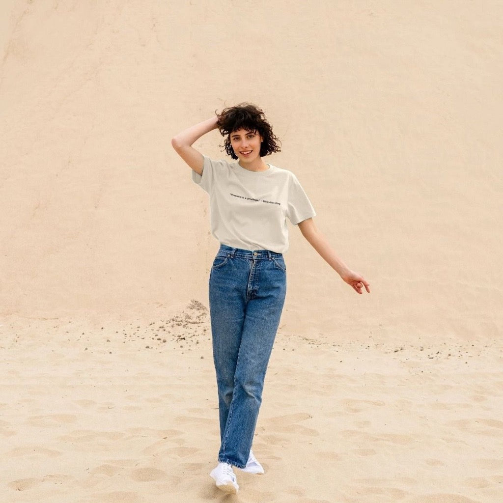 Woman standing on sand wearing a white t-shirt and blue jeans.
