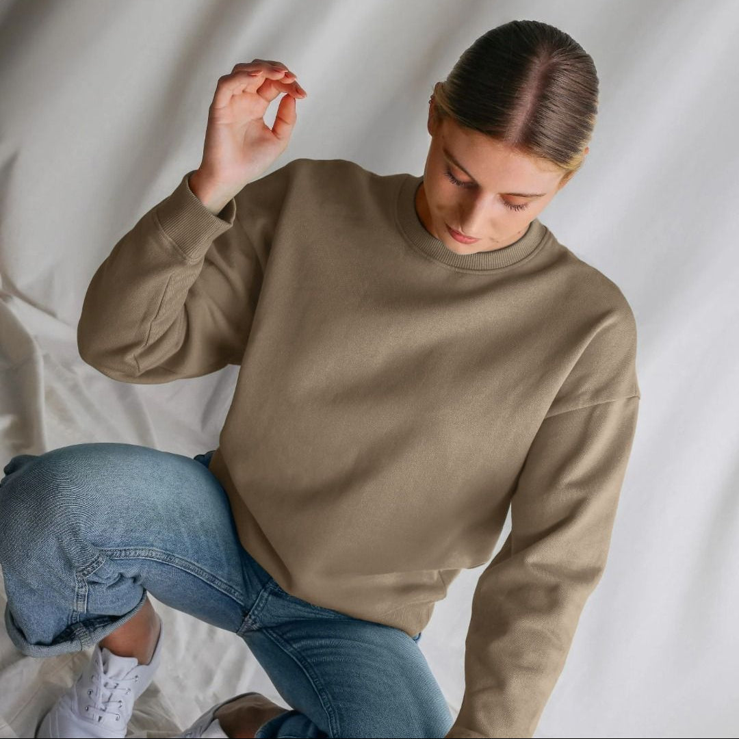 Person wearing a beige sweatshirt and blue jeans against a plain background