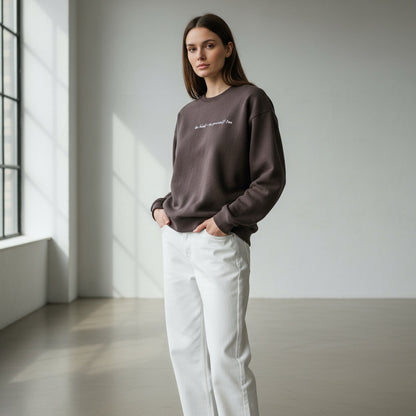 Woman wearing a dark brown sweatshirt and white pants in a minimalistic room.