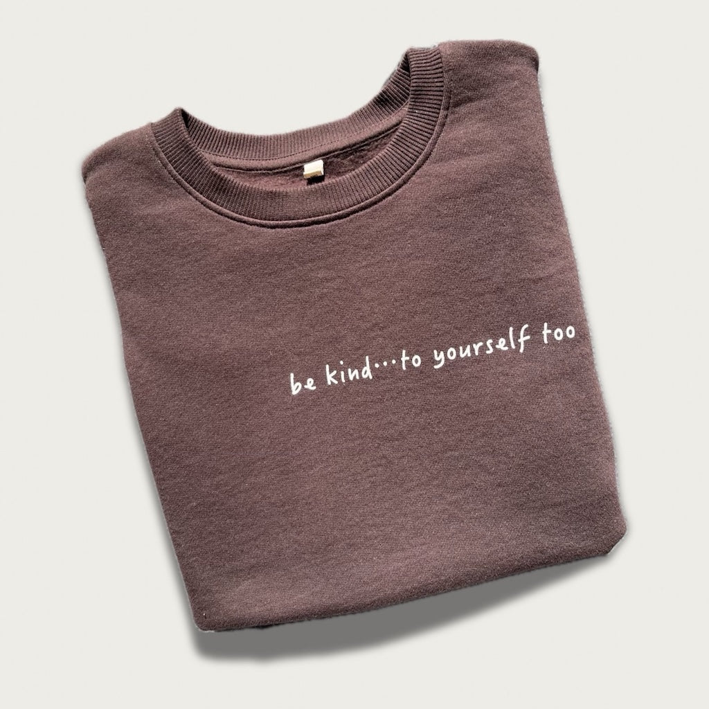 Folded brown sweatshirt with 'be kind...to yourself too' text