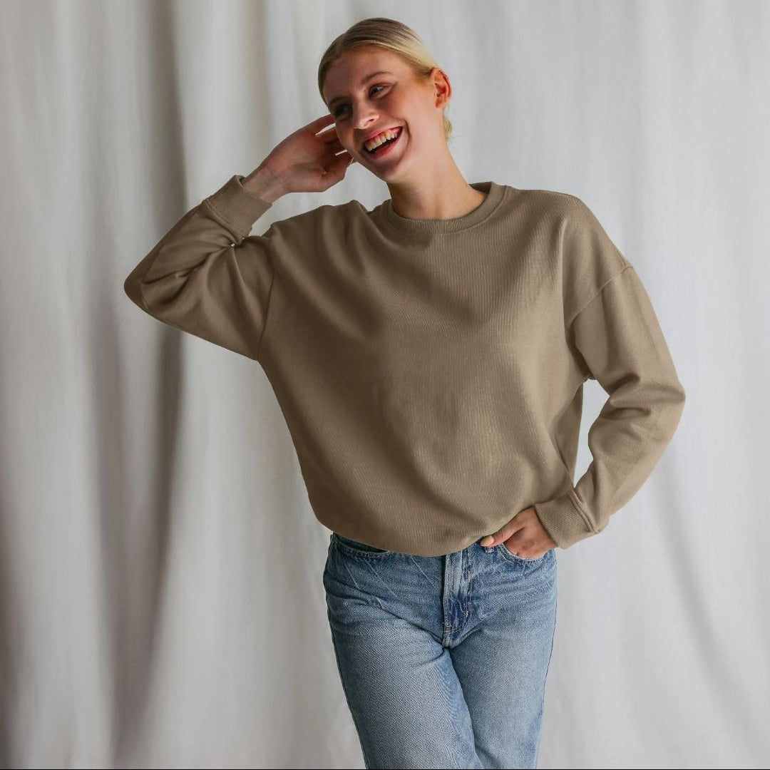 Person wearing a beige sweatshirt and blue jeans against a plain background