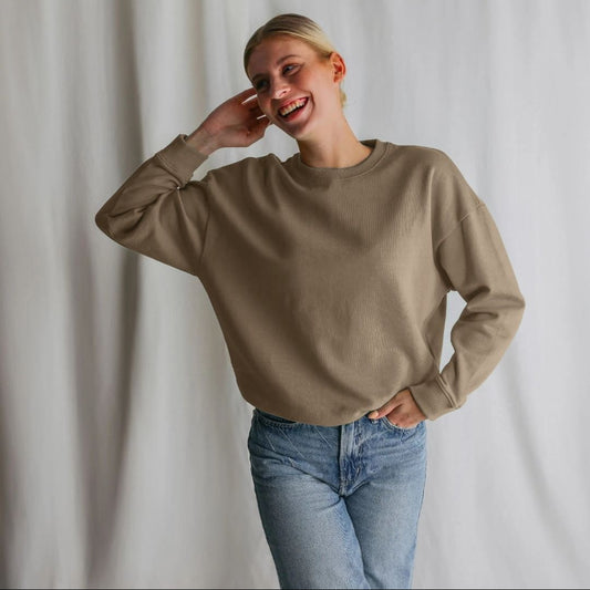 Person wearing a beige sweatshirt and blue jeans against a plain background